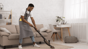 A Man In An Apron Vacuuming A Carpet